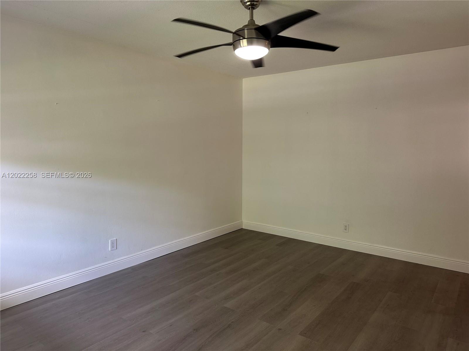 An empty room features white walls, dark wood-look flooring, and a ceiling fan — 3700 Harrison St # 15A, Hollywood FL 33021, HOLLYWOOD, FL
