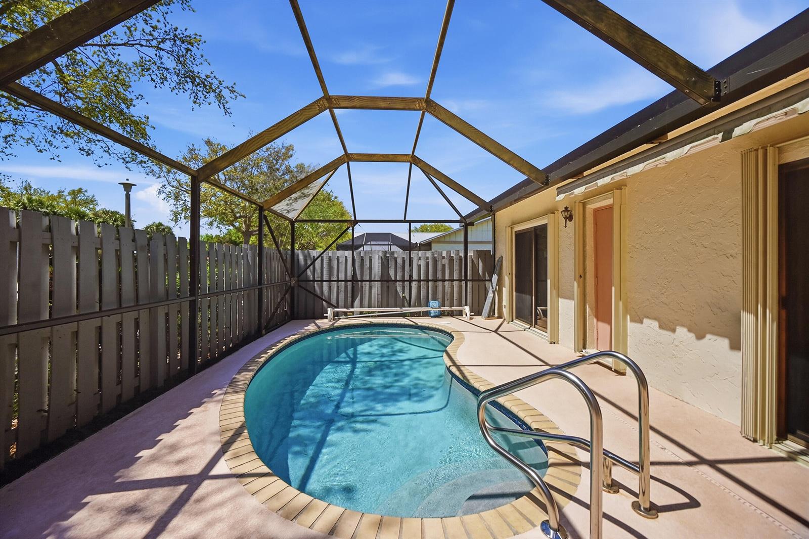 A kidney-shaped swimming pool sits inside a screened-in patio enclosure with a wooden fence — 8853 Andy Court # A, Boynton Beach FL 33436, BOYNTON BEACH, FL