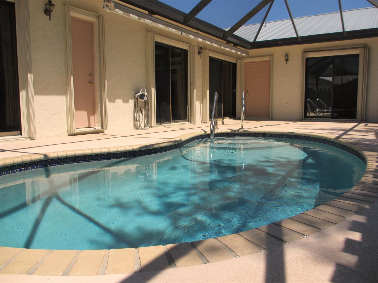 A swimming pool with a brick coping sits on a patio enclosed by a screen — 8853 Andy Court # A, Boynton Beach FL 33436, BOYNTON BEACH, FL