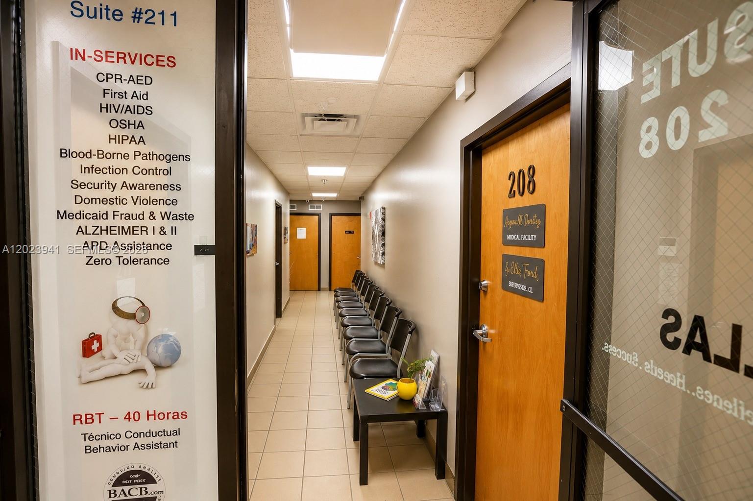 A hallway with a row of chairs leads to two wooden doors in an office building — 4355 W 16th Ave # 211, Hialeah FL 33012, HIALEAH, FL