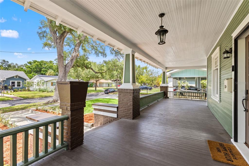 A covered front porch features wooden flooring, brick columns, and green railings — 120 W COMANCHE AVENUE, TAMPA, FL