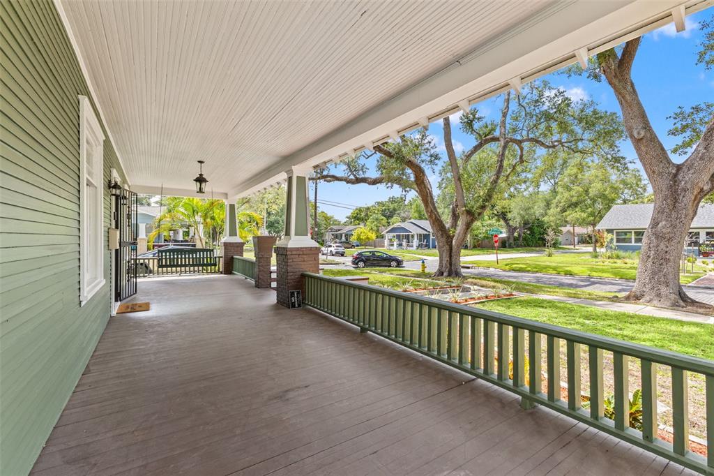 A wide, covered wooden porch features green railings, a porch swing, and brick-based columns — 120 W COMANCHE AVENUE, TAMPA, FL
