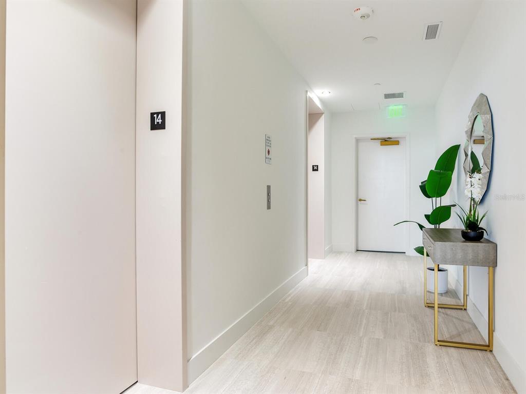 A hallway on the 14th floor features light wood-look flooring, an elevator, and a console table — 3015 S YSABELLA AVENUE UNIT 1403, TAMPA, FL