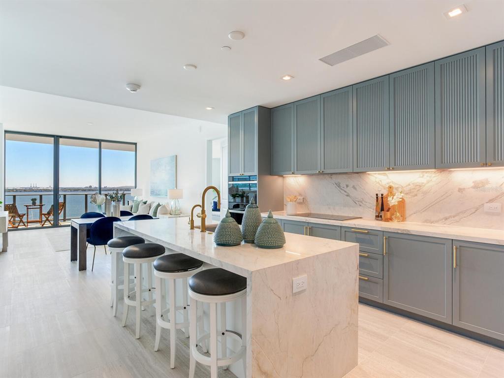 A modern kitchen features blue cabinets, a marble island with bar stools, and water views — 3015 S YSABELLA AVENUE UNIT 1403, TAMPA, FL