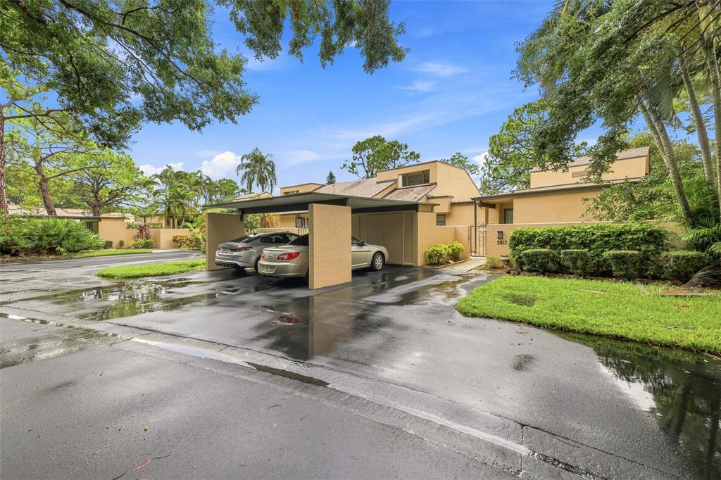 A tan townhouse exterior features a covered carport with two parked cars on a wet driveway — 3813 FISHING TRAIL UNIT 62, SARASOTA, FL
