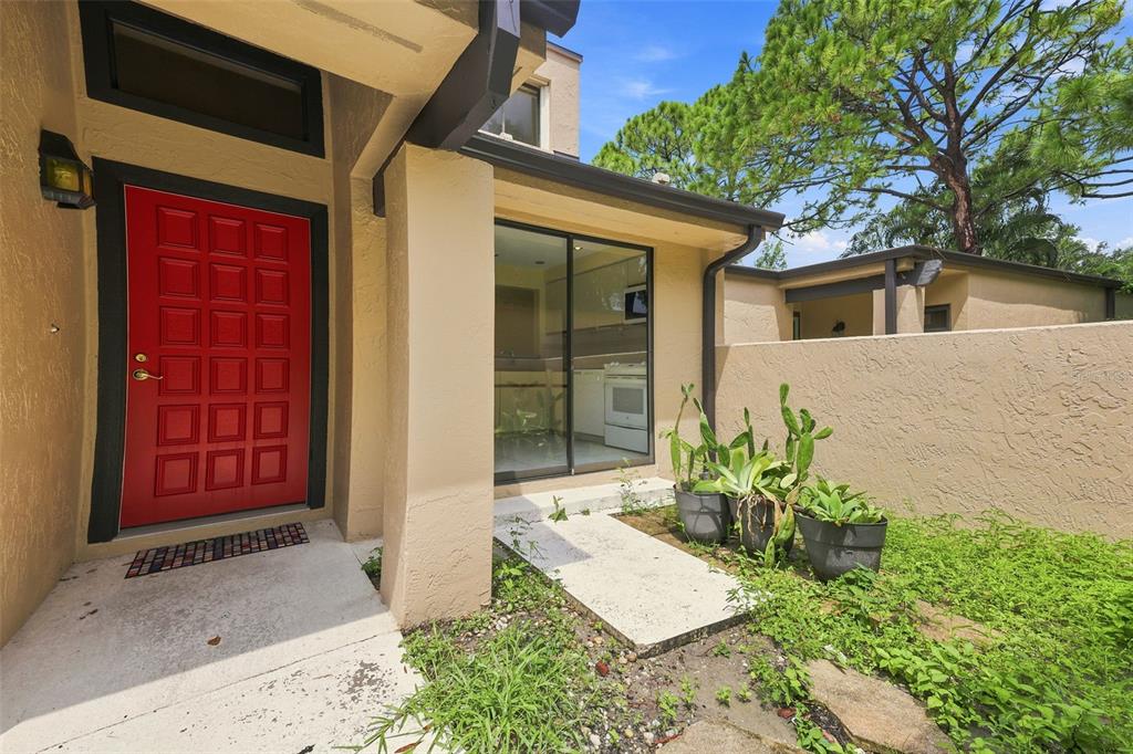 A red front door and sliding glass doors lead into a home with exterior stucco walls — 3813 FISHING TRAIL UNIT 62, SARASOTA, FL