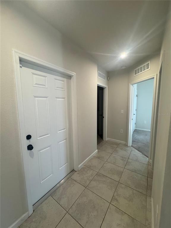 An interior hallway features light-colored tile flooring, a white door, and two open doorways — 1666 AMBAR COURT, WINTER HAVEN, FL