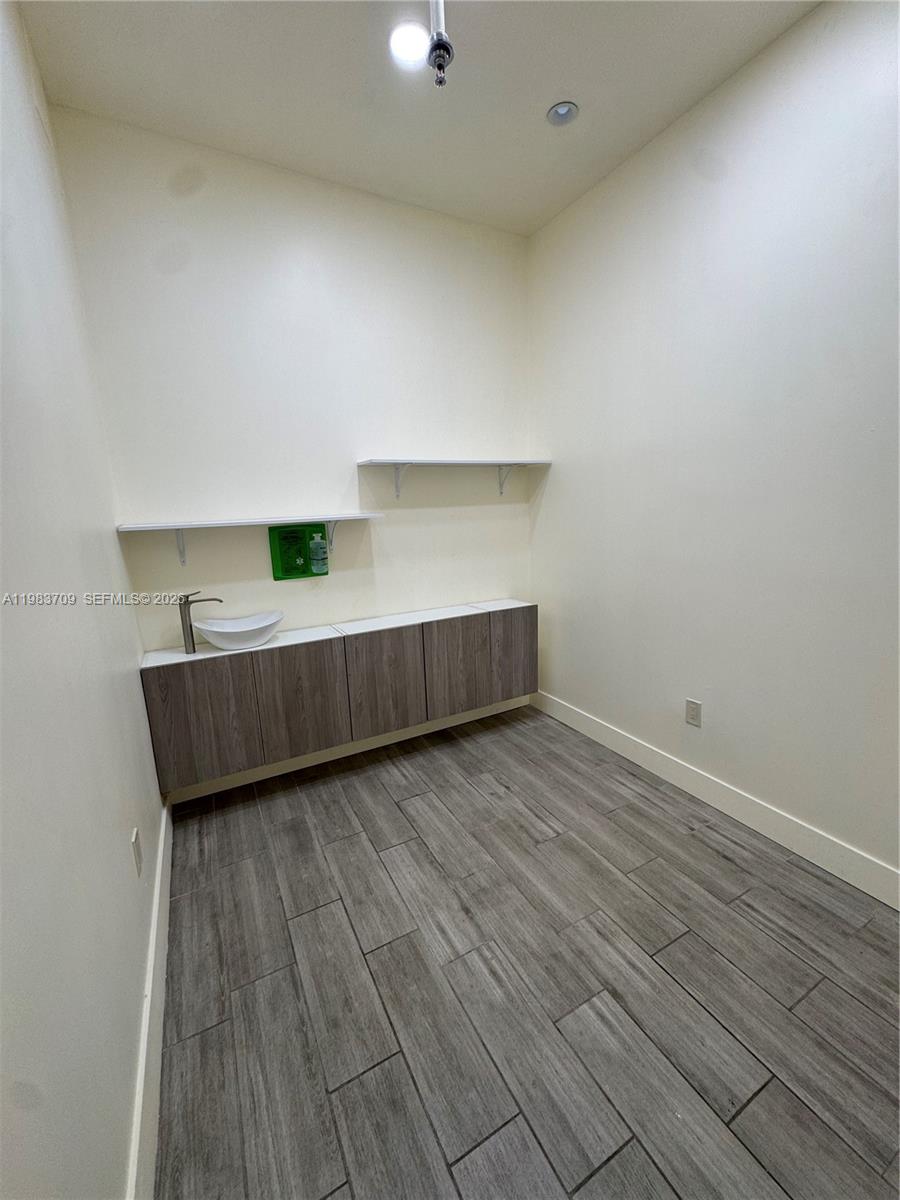 A small room features wood-look tile flooring, wall-mounted cabinets, a vessel sink, and open shelving — 110 Washington Ave # 7, Miami Beach FL 33139, MIAMI BEACH, FL