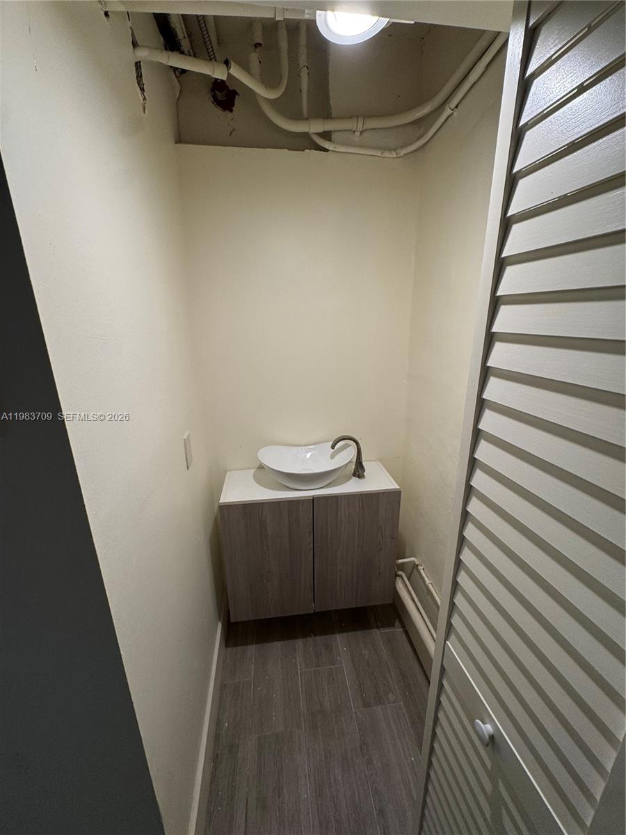 A small bathroom features a vessel sink on a wood-toned vanity and exposed ceiling pipes — 110 Washington Ave # 7, Miami Beach FL 33139, MIAMI BEACH, FL