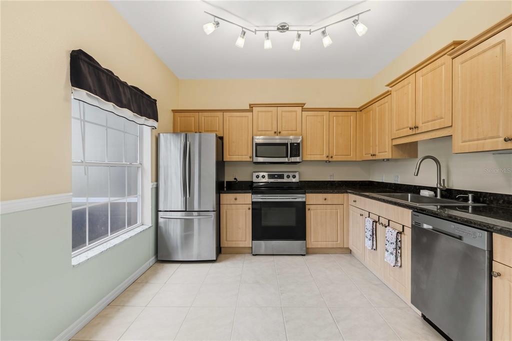 A kitchen with light wood cabinets, stainless steel appliances, dark countertops, and tile flooring — 7604 PLANTATION CIRCLE UNIT 7604, UNIVERSITY PARK, FL