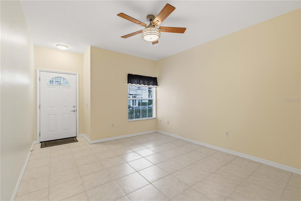 An empty room with beige walls, tile flooring, a ceiling fan, and a front door — 7604 PLANTATION CIRCLE UNIT 7604, UNIVERSITY PARK, FL