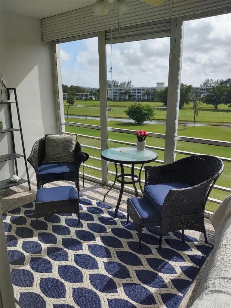 A sunroom features wicker chairs, a small glass table, and a blue patterned rug — 2691 S Course Drive # 409, Pompano Beach FL 33069, POMPANO BEACH, FL