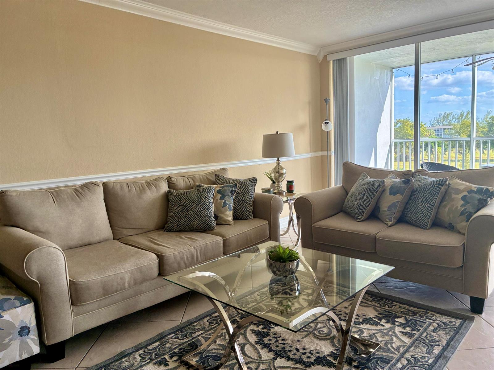 A living room features two beige sofas, a glass coffee table, and a balcony view — 2691 S Course Drive # 409, Pompano Beach FL 33069, POMPANO BEACH, FL