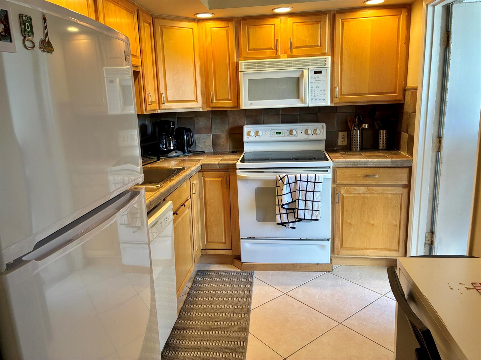 A kitchen features light wood cabinets, white appliances, tiled countertops, and a tiled floor — 2691 S Course Drive # 409, Pompano Beach FL 33069, POMPANO BEACH, FL