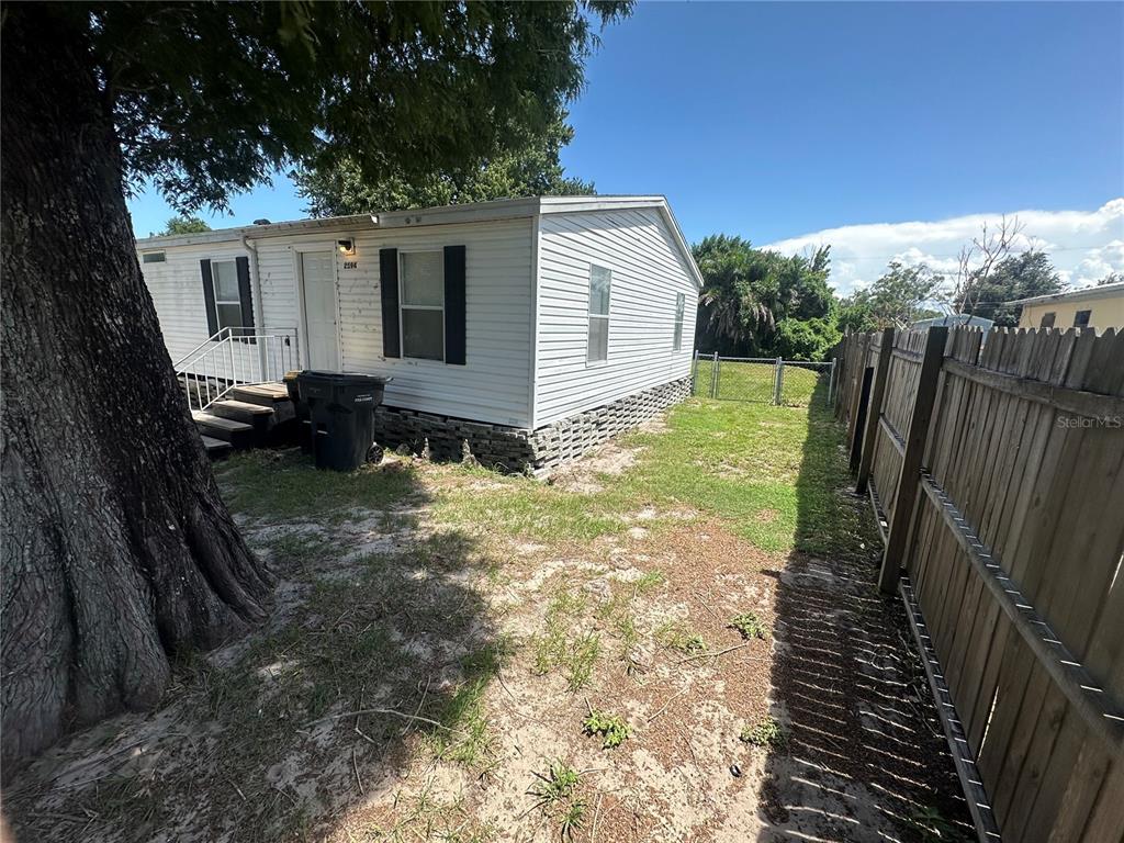 A white mobile home with a wooden fence and a large tree in the yard — 2594 MCINTOSH DRIVE, LAKELAND, FL