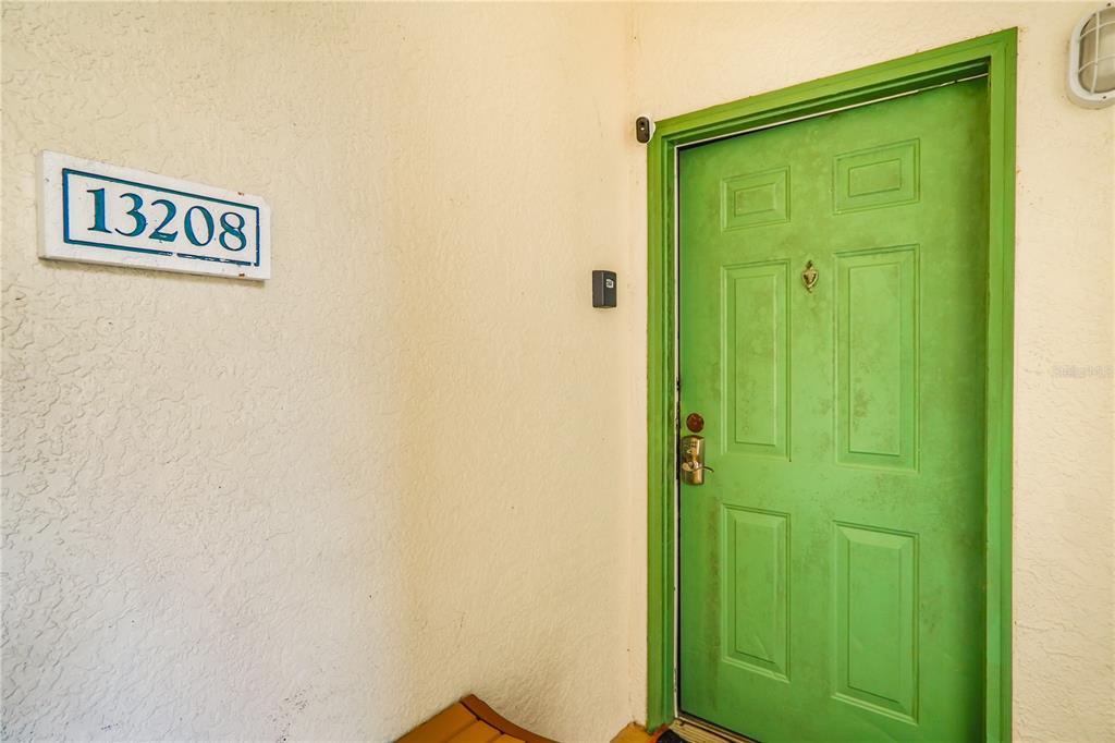 A bright green front door is set into a textured beige exterior wall — 8836 DUNES COURT UNIT 208, KISSIMMEE, FL