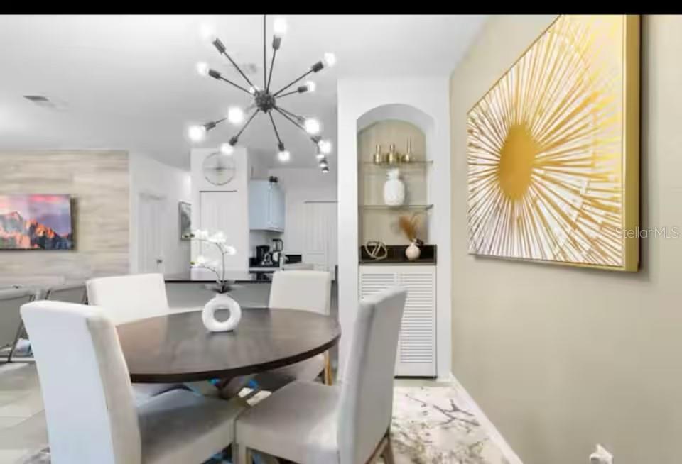 A dining area features a round wooden table, four white chairs, and a modern chandelier — 8836 DUNES COURT UNIT 208, KISSIMMEE, FL