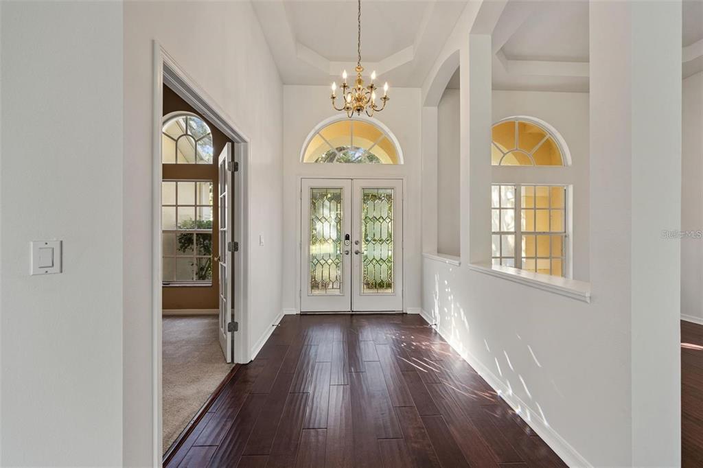 A bright entryway features dark wood flooring, a chandelier, and double glass-paneled front doors — 1452 KENSINGTON WOODS DRIVE, LUTZ, FL