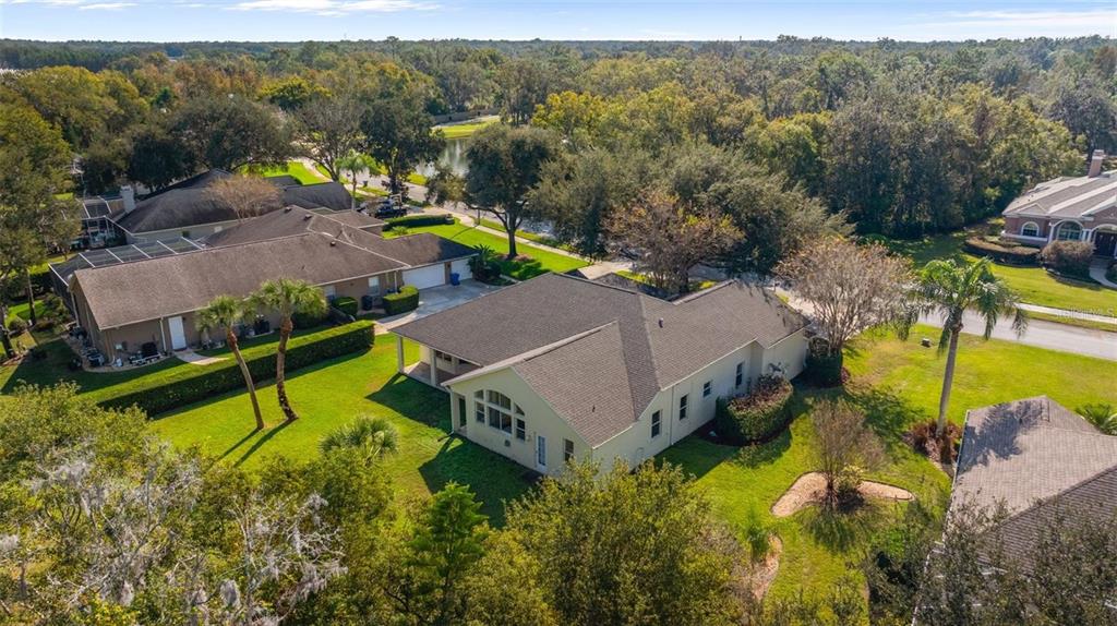 An aerial view shows a suburban house with a large roof and backyard lawn — 1452 KENSINGTON WOODS DRIVE, LUTZ, FL