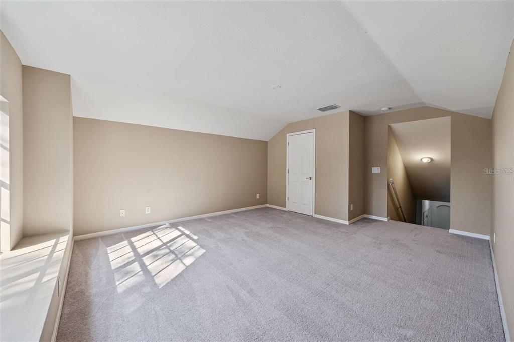 An empty carpeted room with beige walls, a window seat, and a doorway to stairs — 1452 KENSINGTON WOODS DRIVE, LUTZ, FL