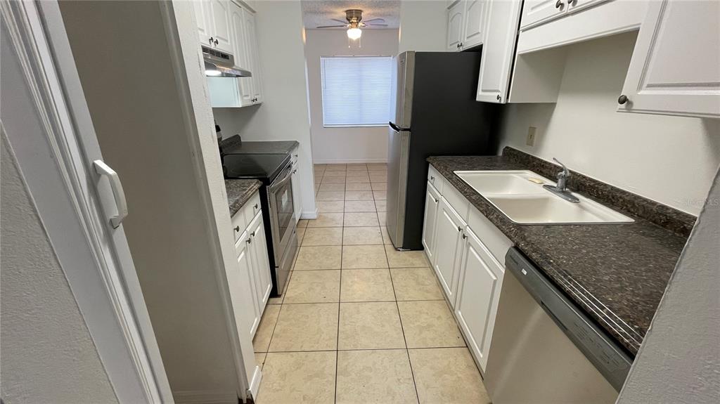 A galley kitchen features white cabinets, dark countertops, stainless steel appliances, and beige tile flooring — 7502 NEEDLE LEAF PLACE UNIT 66, TAMPA, FL
