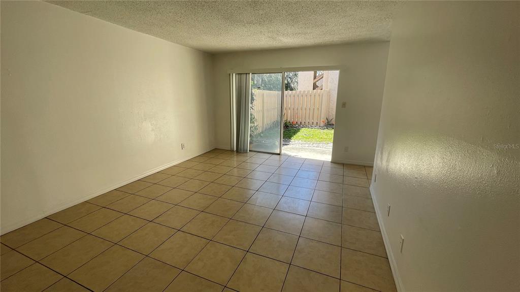 An empty room with beige tile flooring and a sliding glass door leading outside — 7502 NEEDLE LEAF PLACE UNIT 66, TAMPA, FL