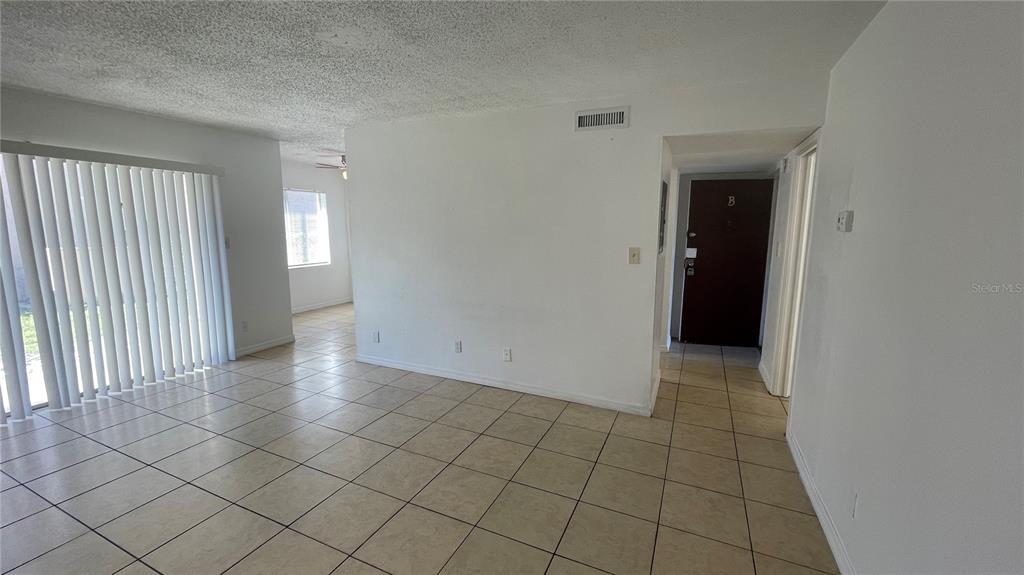 An empty living area features white walls, beige tile flooring, and a sliding glass door — 7502 NEEDLE LEAF PLACE UNIT 66, TAMPA, FL