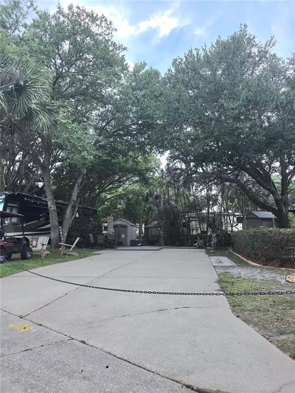A concrete driveway leads toward a shaded campsite with a parked RV and small shed — 206 LONGHORN DRIVE, LAKE WALES, FL