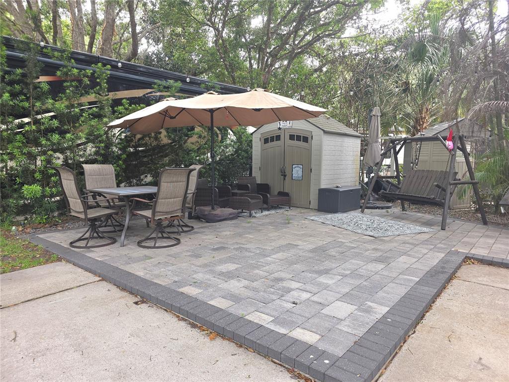 A paved patio features a dining set with an umbrella, a storage shed, and a swing — 206 LONGHORN DRIVE, LAKE WALES, FL