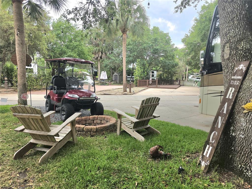 A golf cart and two wooden chairs sit on a lawn near a fire pit — 206 LONGHORN DRIVE, LAKE WALES, FL