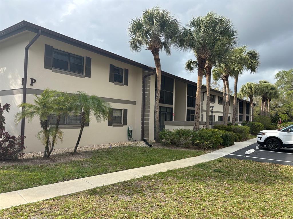 A two-story apartment building exterior features beige stucco walls, dark shutters, and palm trees — 1515 FORREST NELSON BOULEVARD UNIT P208, PORT CHARLOTTE, FL
