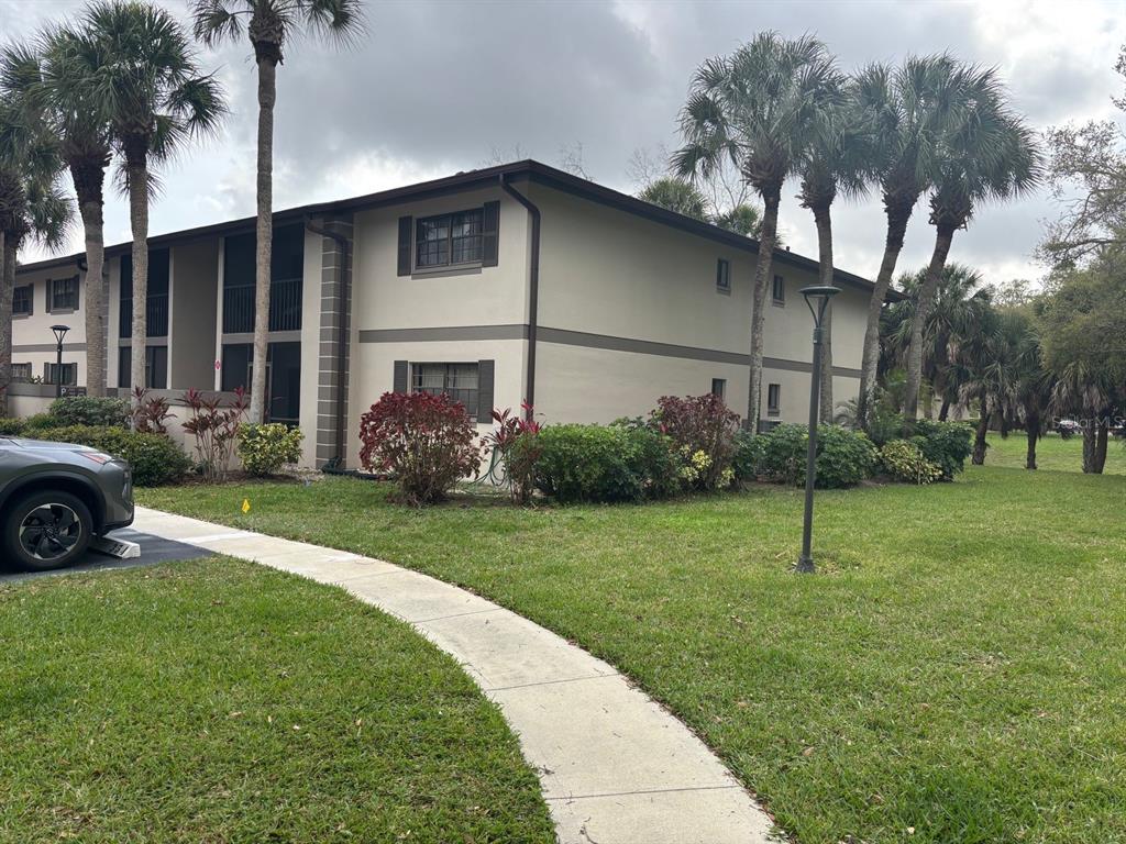 A two-story apartment building with beige siding and palm trees sits on a grassy lawn — 1515 FORREST NELSON BOULEVARD UNIT P208, PORT CHARLOTTE, FL