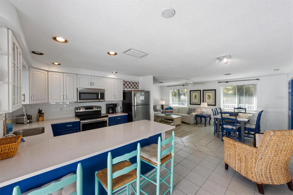 A kitchen with white cabinets and blue lower cupboards opens into a dining and living area — 5807 DE PALMAS AVENUE, HOLMES BEACH, FL