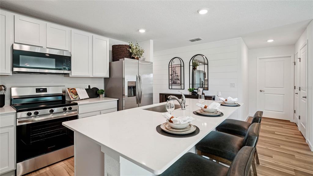 A modern kitchen features white cabinets, stainless steel appliances, and a large quartz-topped island — 7836 SW 46TH COURT, OCALA, FL