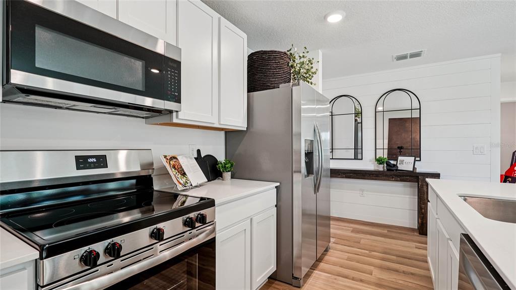 A kitchen features white cabinets, stainless steel appliances, and a wood-look floor — 7836 SW 46TH COURT, OCALA, FL