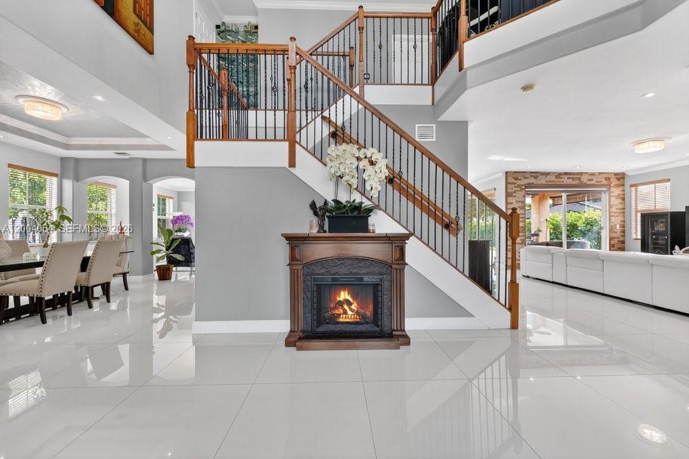 A grand foyer features a central fireplace, a wooden staircase, and white tile flooring — 15465 SW 117th St, Miami FL 33196, MIAMI, FL
