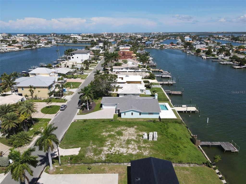 An aerial view shows a vacant waterfront lot next to a house with a pool — 11125 4TH ST E, TREASURE ISLAND, FL