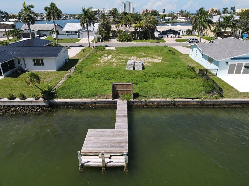 An aerial view shows a vacant waterfront lot with a wooden dock and surrounding houses — 11125 4TH ST E, TREASURE ISLAND, FL
