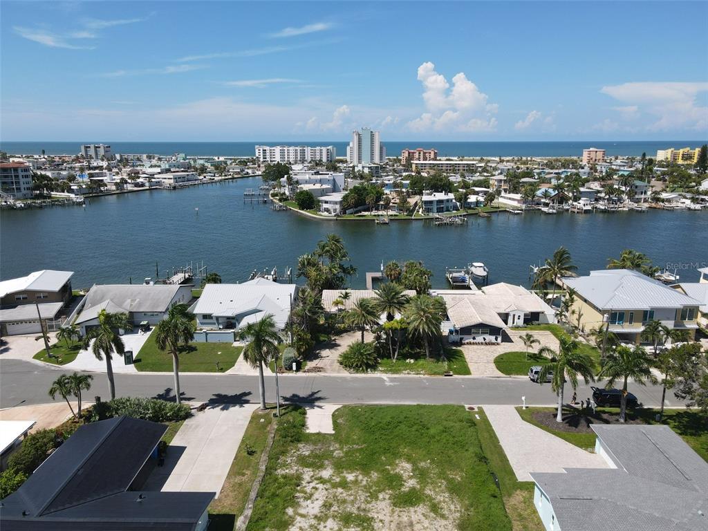 An aerial view shows a vacant lot in the foreground facing a canal and ocean — 11125 4TH ST E, TREASURE ISLAND, FL