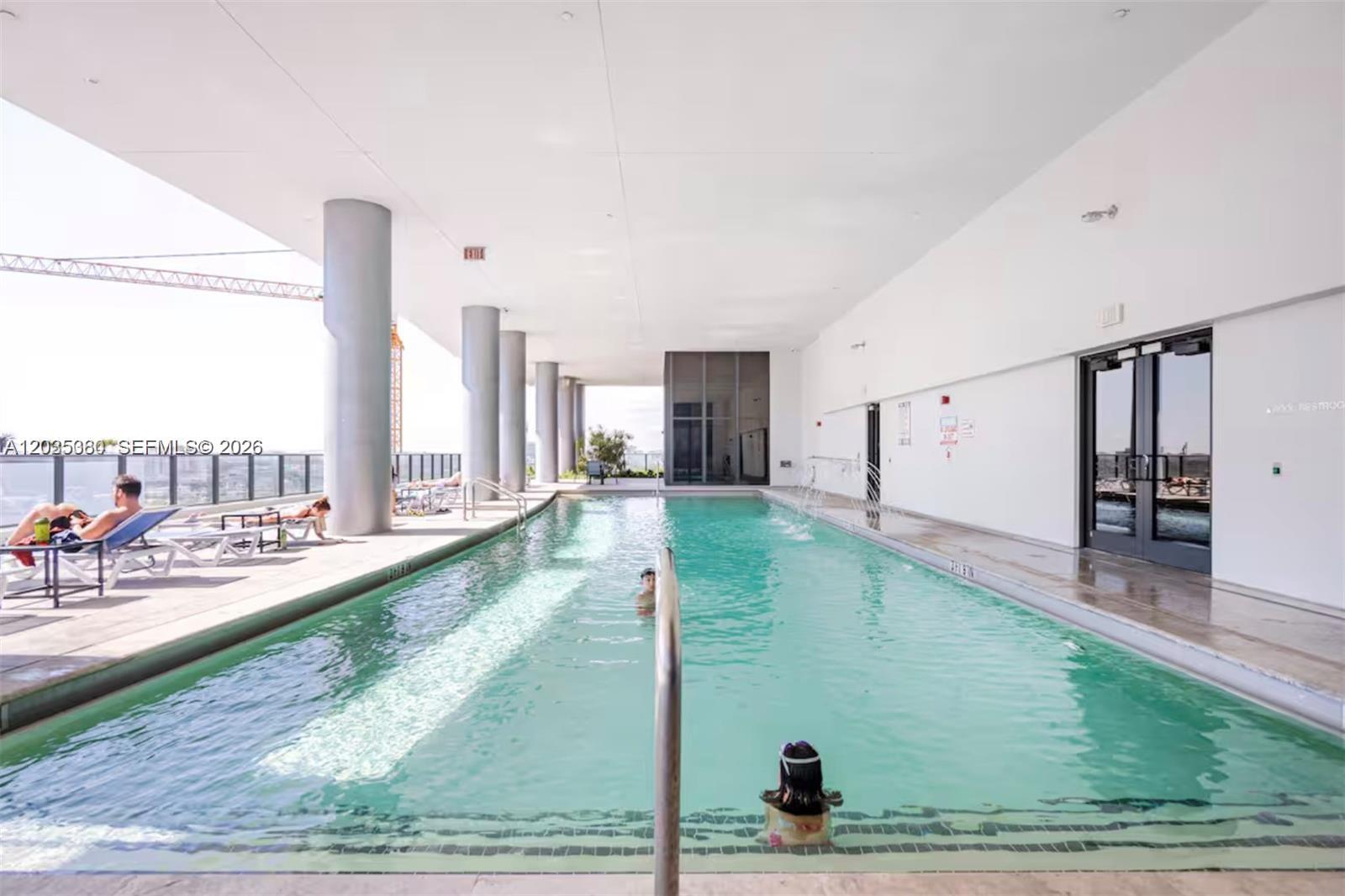 An indoor lap pool with lounge chairs sits under a covered deck with concrete pillars — 1600 NE 1 AVE # 3519, Miami FL 33132, MIAMI, FL