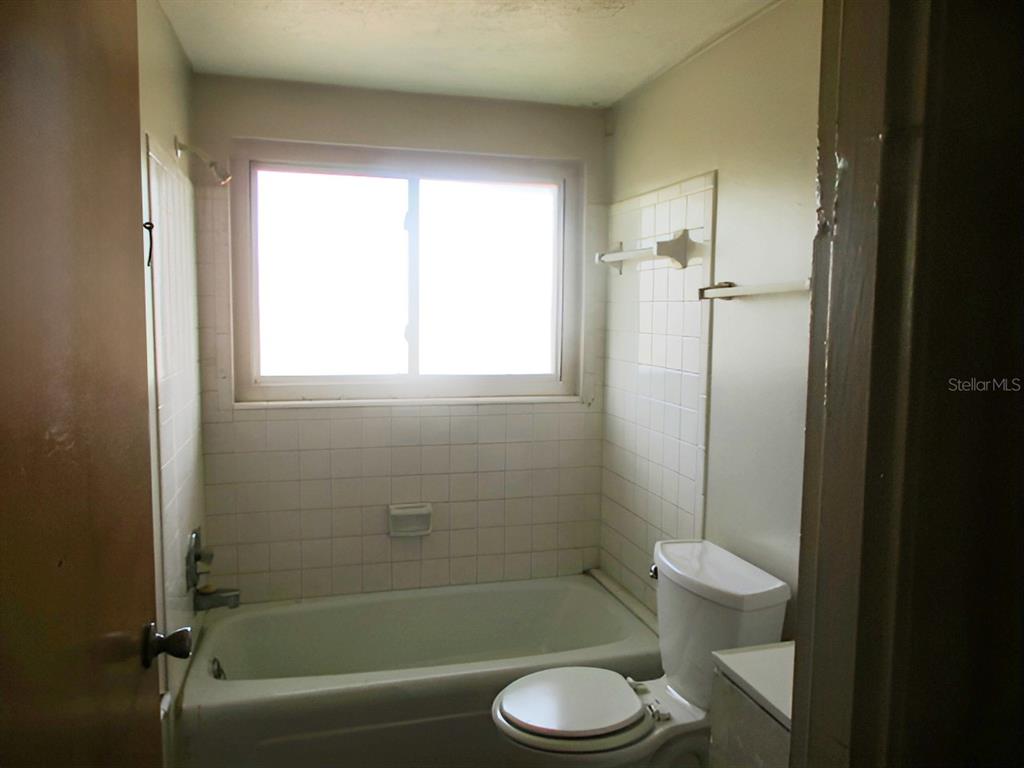 A bathroom features a white bathtub, a toilet, and white tiled walls under a window — 3024 WILLIAMSBURG STREET, SARASOTA, FL