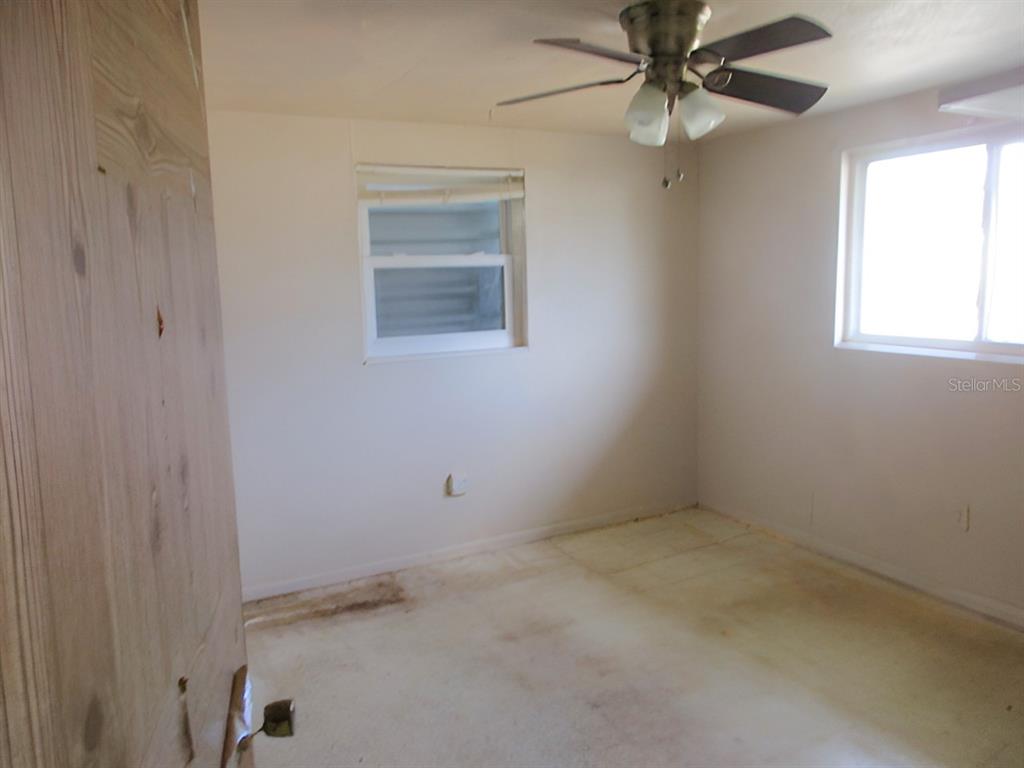 An empty bedroom features beige walls, a ceiling fan, and stained carpeting — 3024 WILLIAMSBURG STREET, SARASOTA, FL