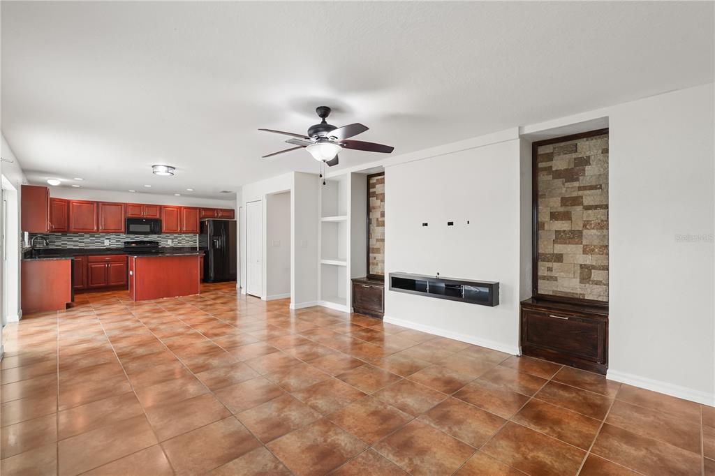 An open-concept living area with tile flooring, a kitchen, and a stone-accented media wall — 656 WASHINGTON WAY, HAINES CITY, FL