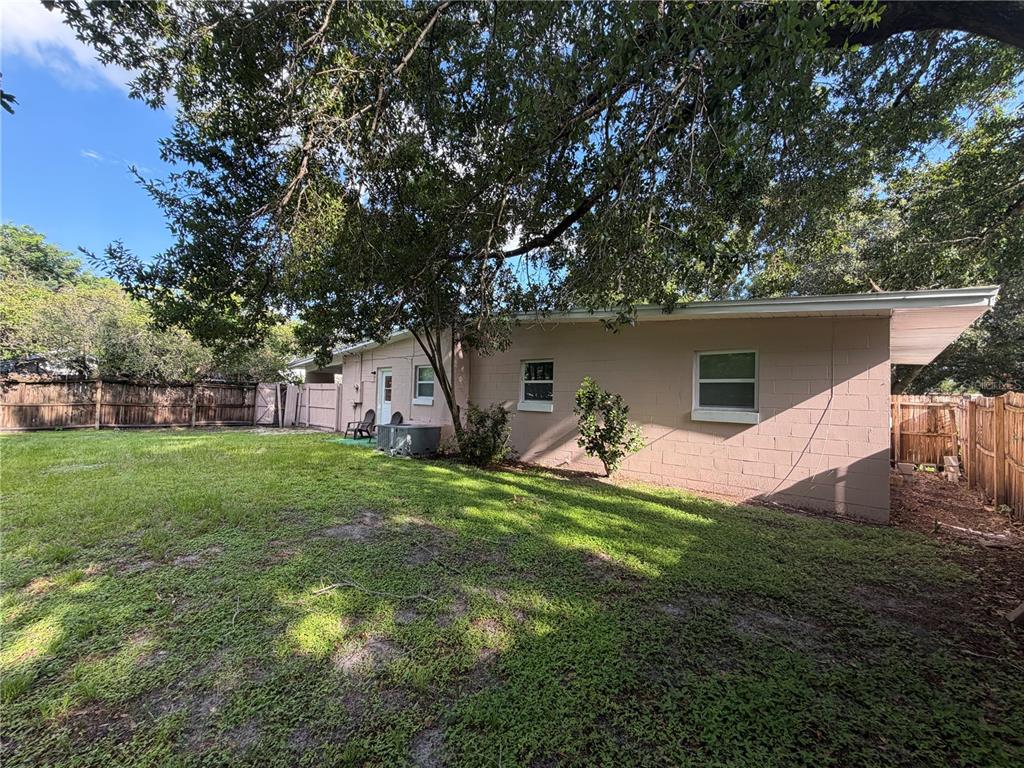 A view of a backyard featuring a pink concrete block house and large shade trees — 6013 CHENANGO LANE, ORLANDO, FL