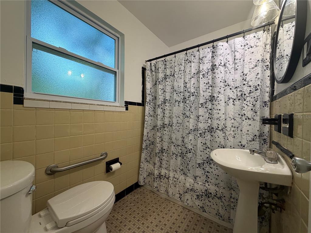 A bathroom features yellow wall tiles, a pedestal sink, a toilet with a grab bar, and a shower — 6013 CHENANGO LANE, ORLANDO, FL