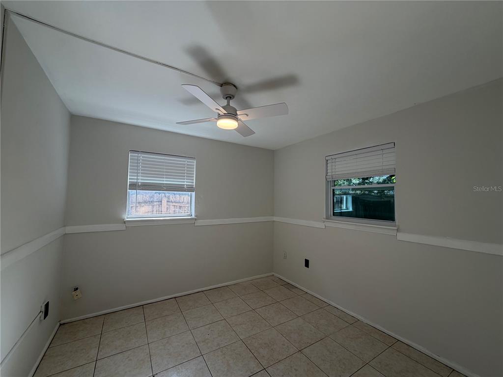 An empty bedroom with light-colored walls, tile flooring, a ceiling fan, and two windows — 6013 CHENANGO LANE, ORLANDO, FL