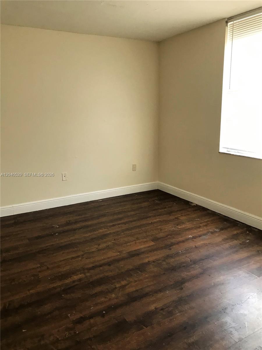An empty room features dark wood-look flooring, beige walls, and a single window with blinds — 10000 NW 80 Ct # 2537, Hialeah Gardens FL 33016, HIALEAH GARDENS, FL
