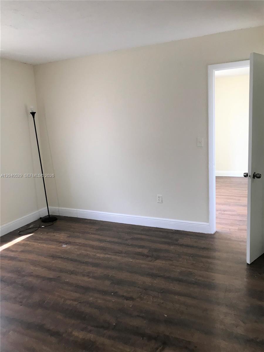 An empty room features beige walls, dark wood-look flooring, and a single floor lamp — 10000 NW 80 Ct # 2537, Hialeah Gardens FL 33016, HIALEAH GARDENS, FL