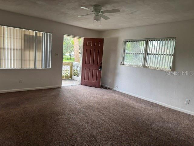 An empty living room features brown carpet, a ceiling fan, and a red exterior door — 2075 HOWELL BRANCH ROAD UNIT 101, MAITLAND, FL