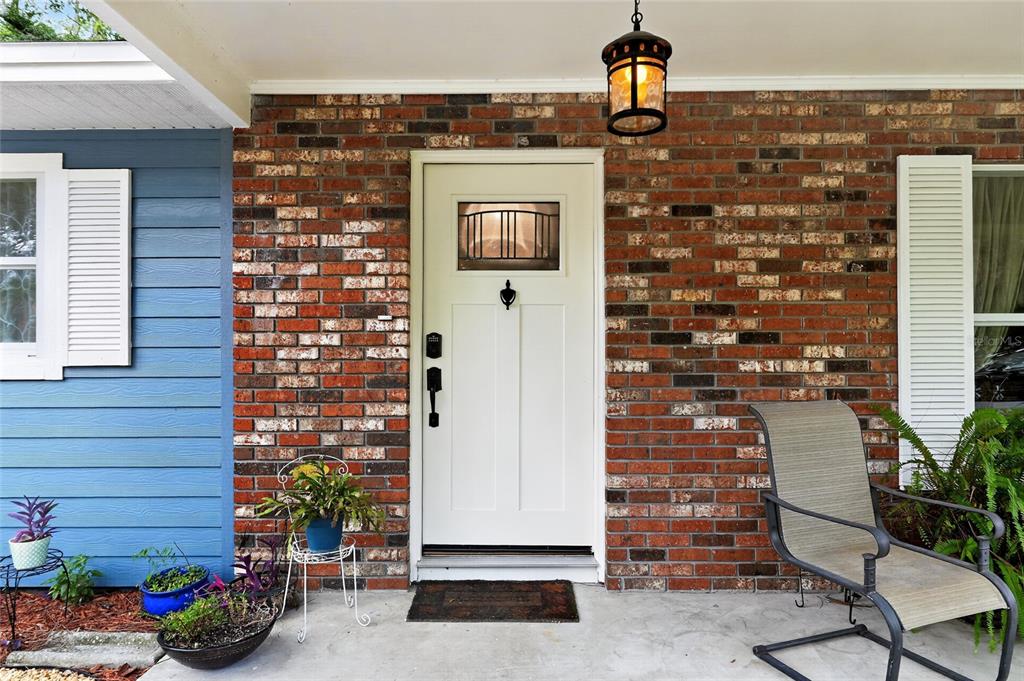 A front porch features a brick exterior, a white door, and a metal chair — 3862 NW 36TH PLACE, GAINESVILLE, FL